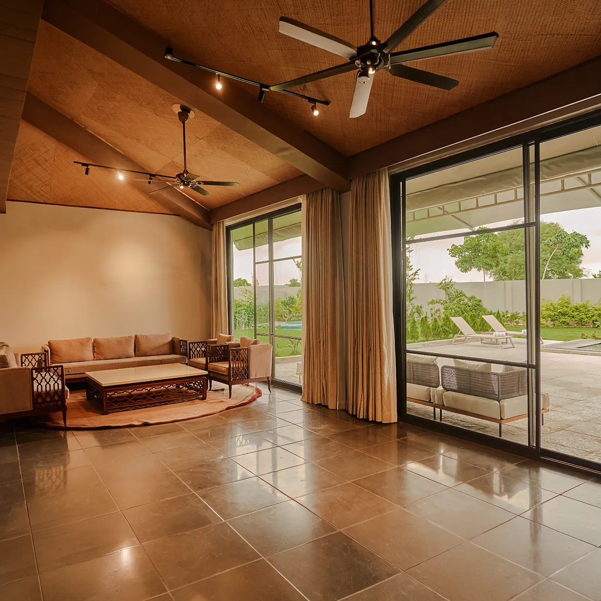 A private villa living room with a timber ceiling, opening onto a pool terrace